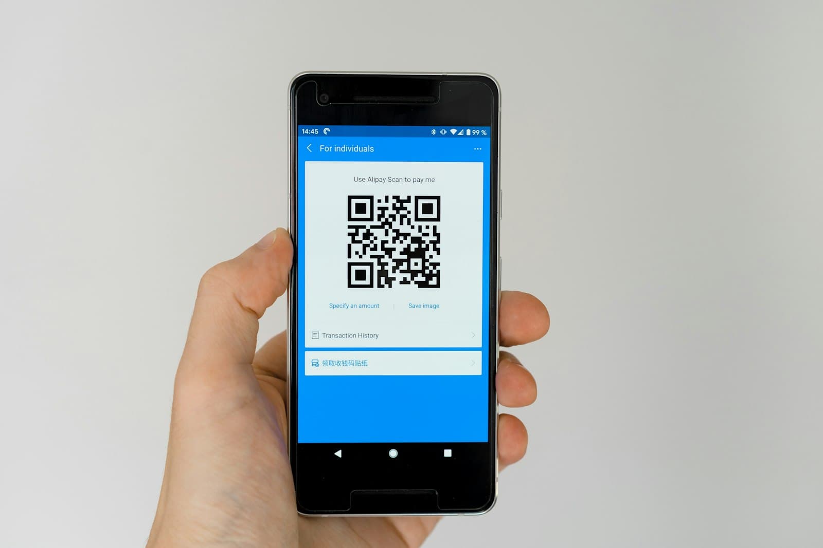 A hand holding a mobile phone showing a QR code
