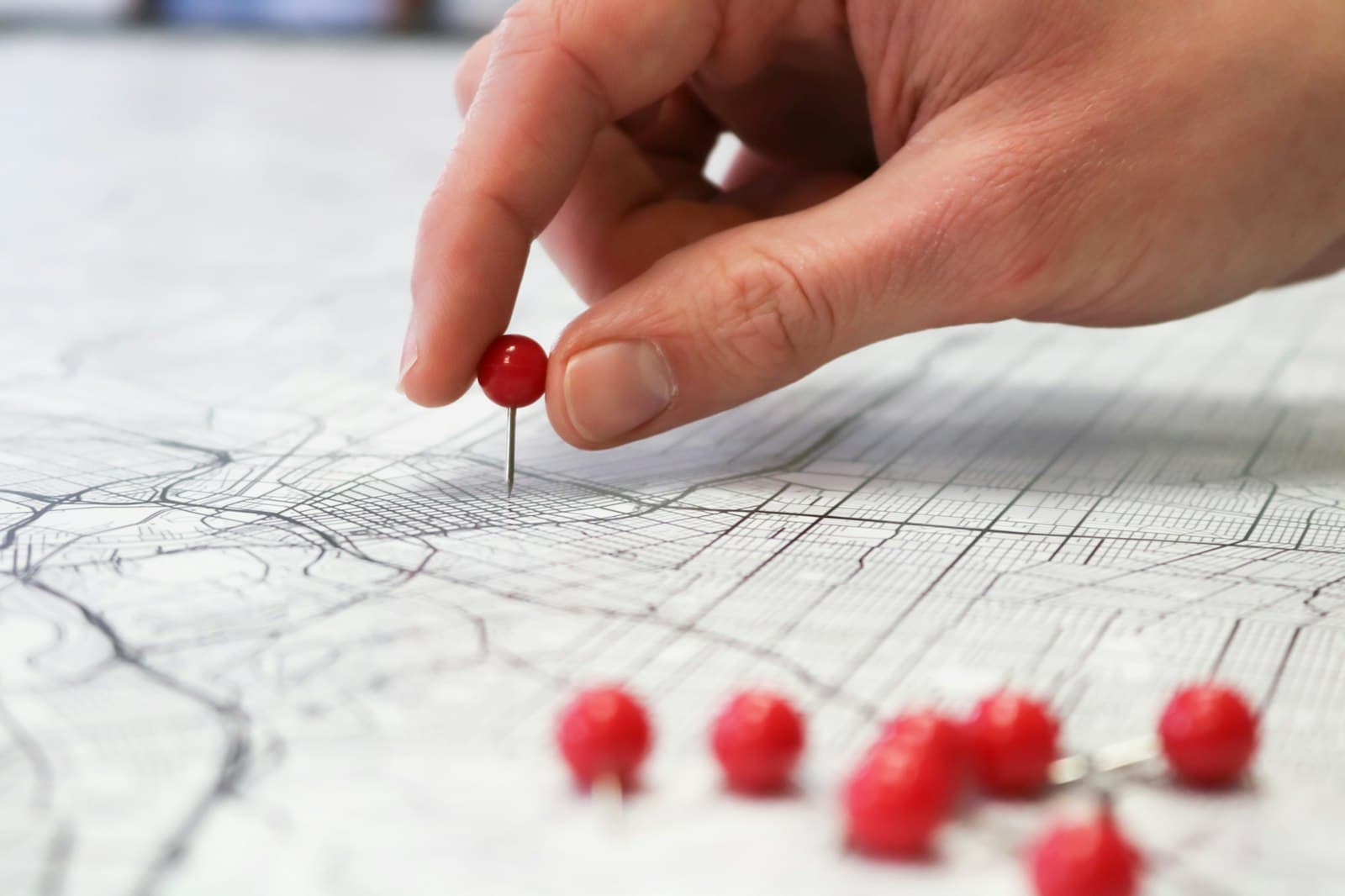 A hand pressing a red pin into a paper street map