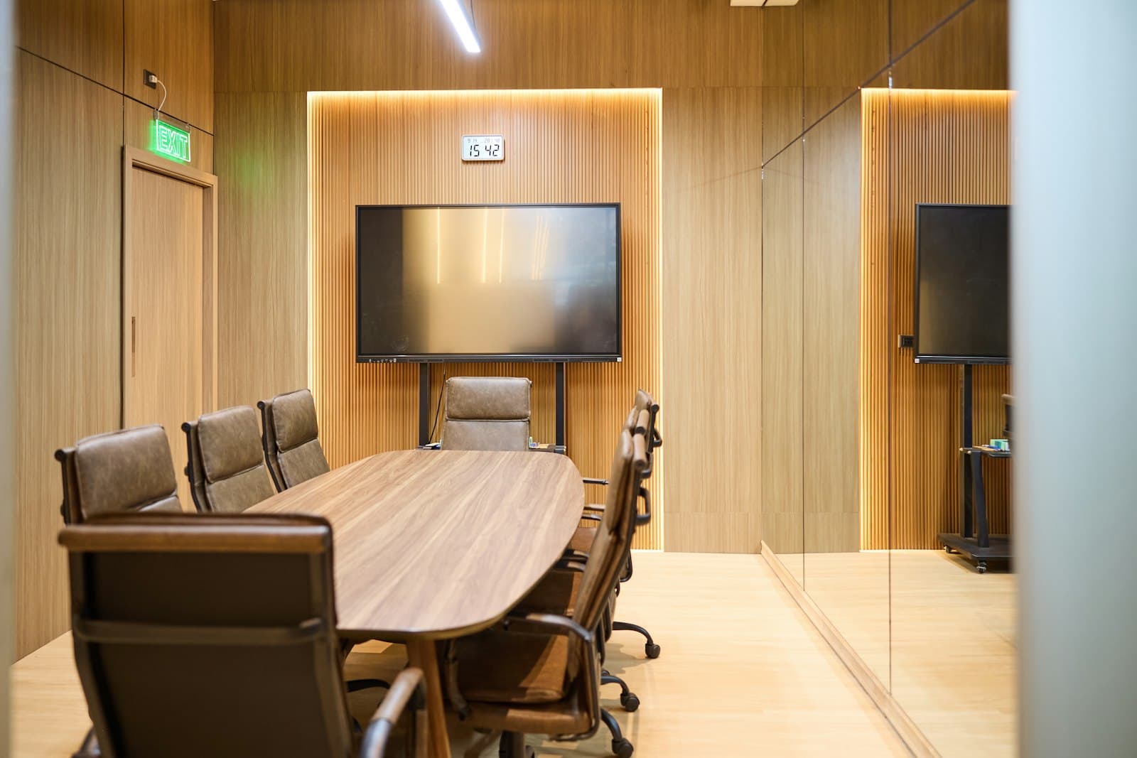 An empty meeting room with an oval table, chairs and a screen on the wall