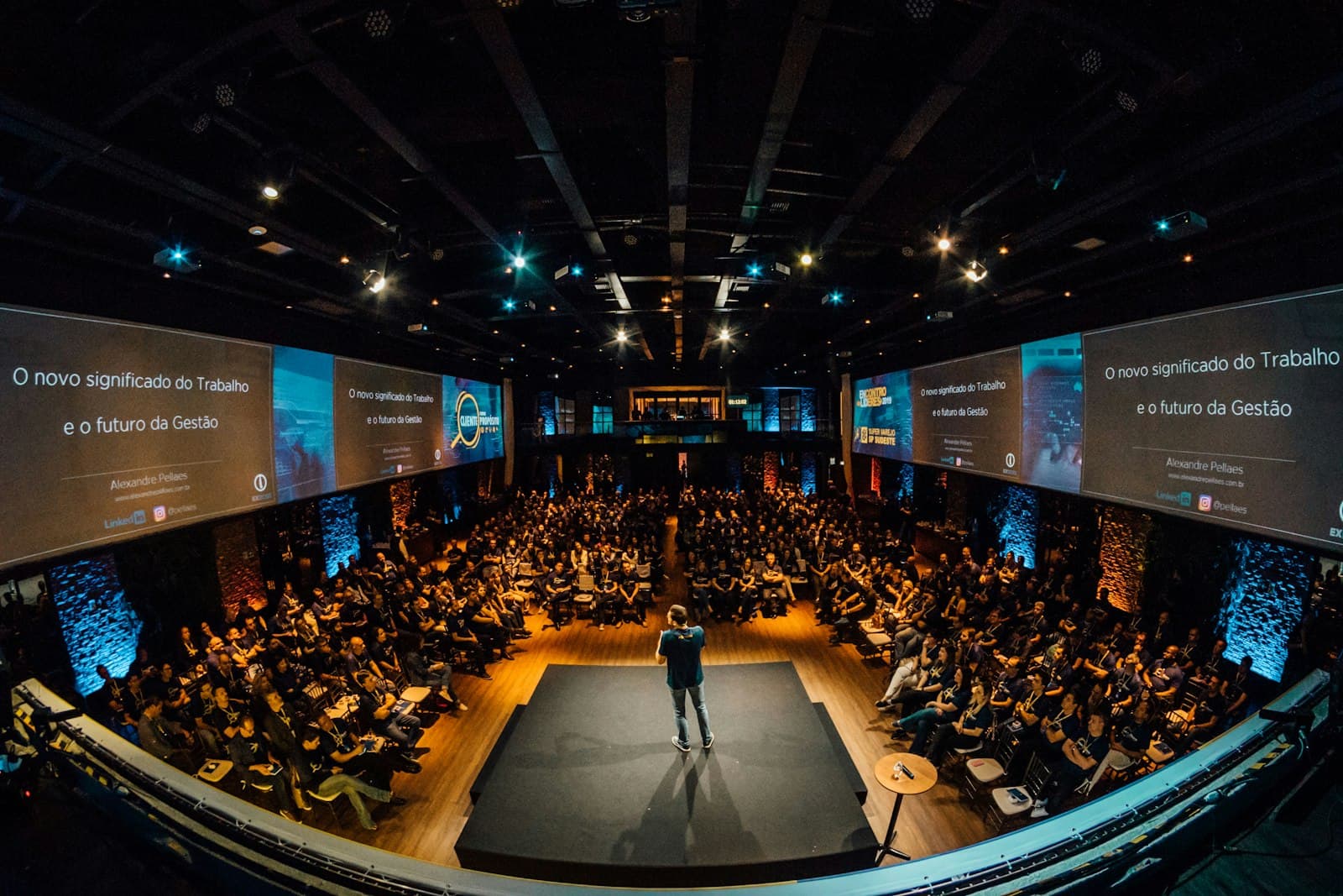 A speaker on a stage in front of a large seated audience